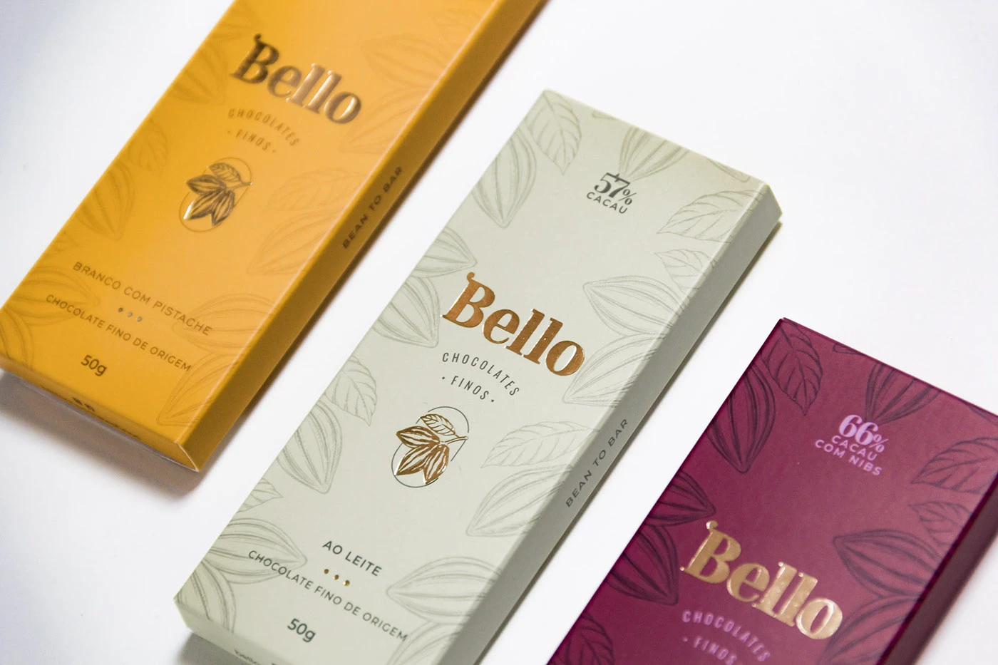 Três barras de chocolate Bello com embalagens ilustradas em mostarda, vinho e oliva
